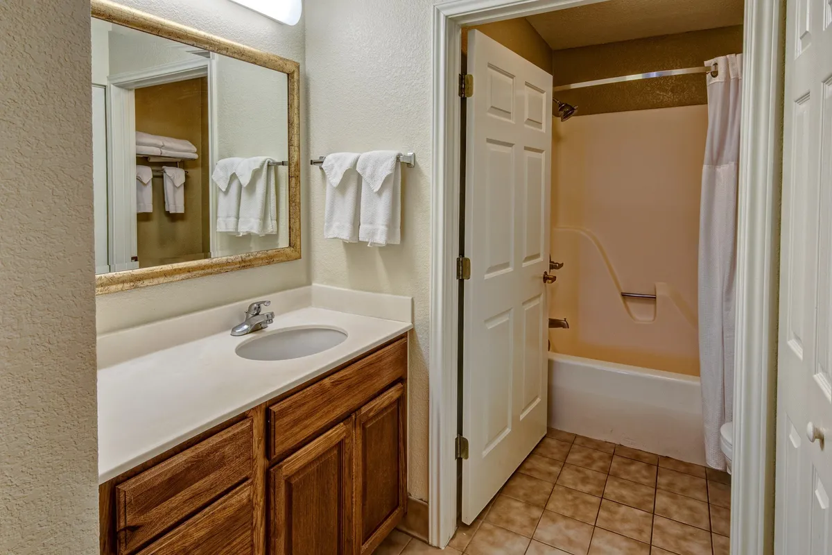 A clean, practical bathroom with a large mirror, modern sink, bathtub, and fluffy towels ready for use. The layout suggests a functional space for personal care and relaxation.