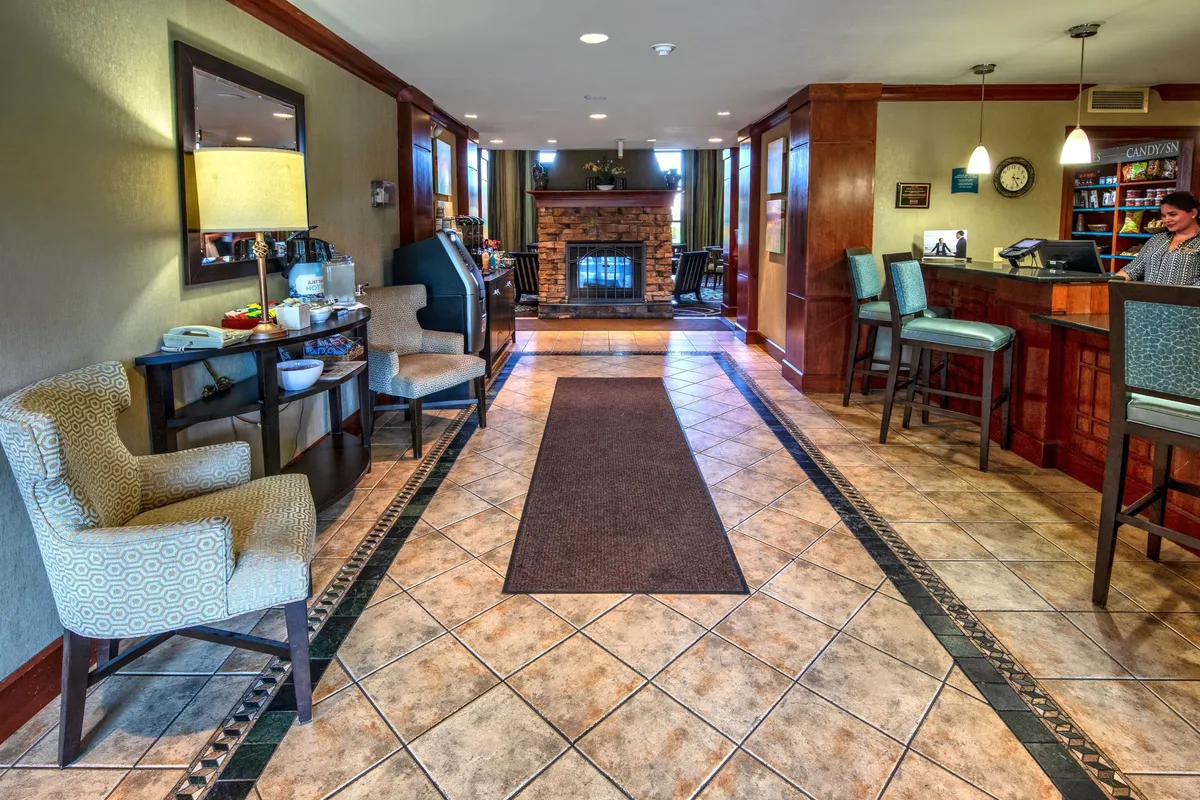A cozy interior scene highlighting the reception area with a glowing fireplace, stylish seating, a decorative mirror, and guests either checking in or relaxing with refreshments. The atmosphere is both inviting and efficient, perfect for busy business travelers.