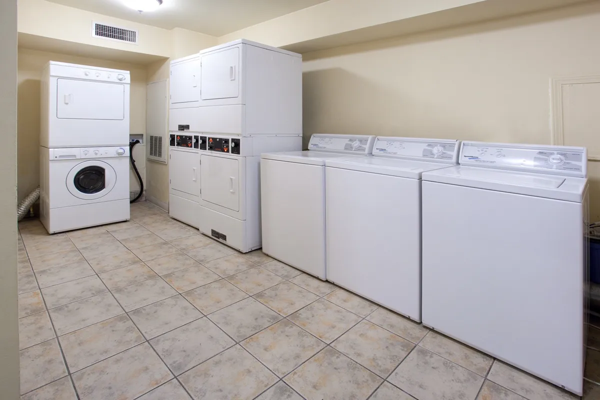A practical laundry room featuring a row of washer and dryer units, clean tile flooring, and storage space for supplies. The design is simple yet efficient, promising ease and convenience for guests.