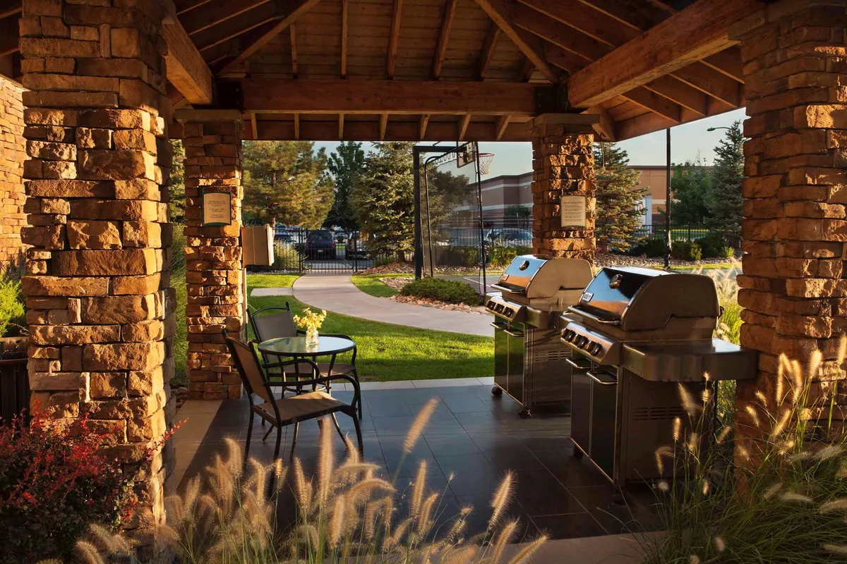 This vibrant exterior shot captures the lively outdoor grills and seating area set amidst a landscaped garden. Families and friends can be seen barbecuing, socializing, and relaxing outdoors, suggesting memorable moments together.