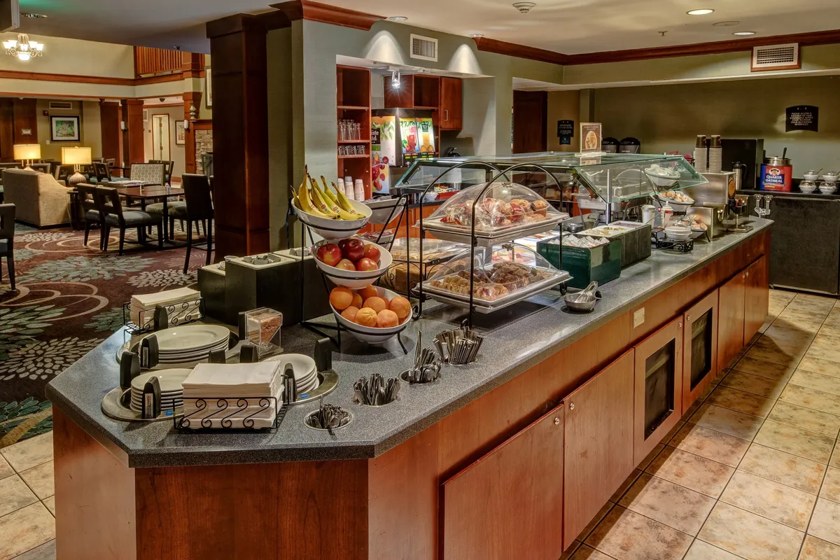 An inviting communal area with a welcoming seating arrangement, a table set for breakfast, fruit baskets, and a coffee station. The space is designed for socializing, sharing meals, or planning the day, highlighted by warm lighting and casual decor.